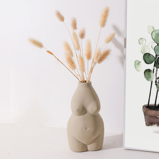 concrete colored womens body vase  with dried grassses next to an Earth to Daisy plant poster