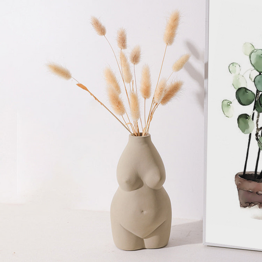 concrete colored womens body vase with dried grassses next to an Earth to Daisy plant poster